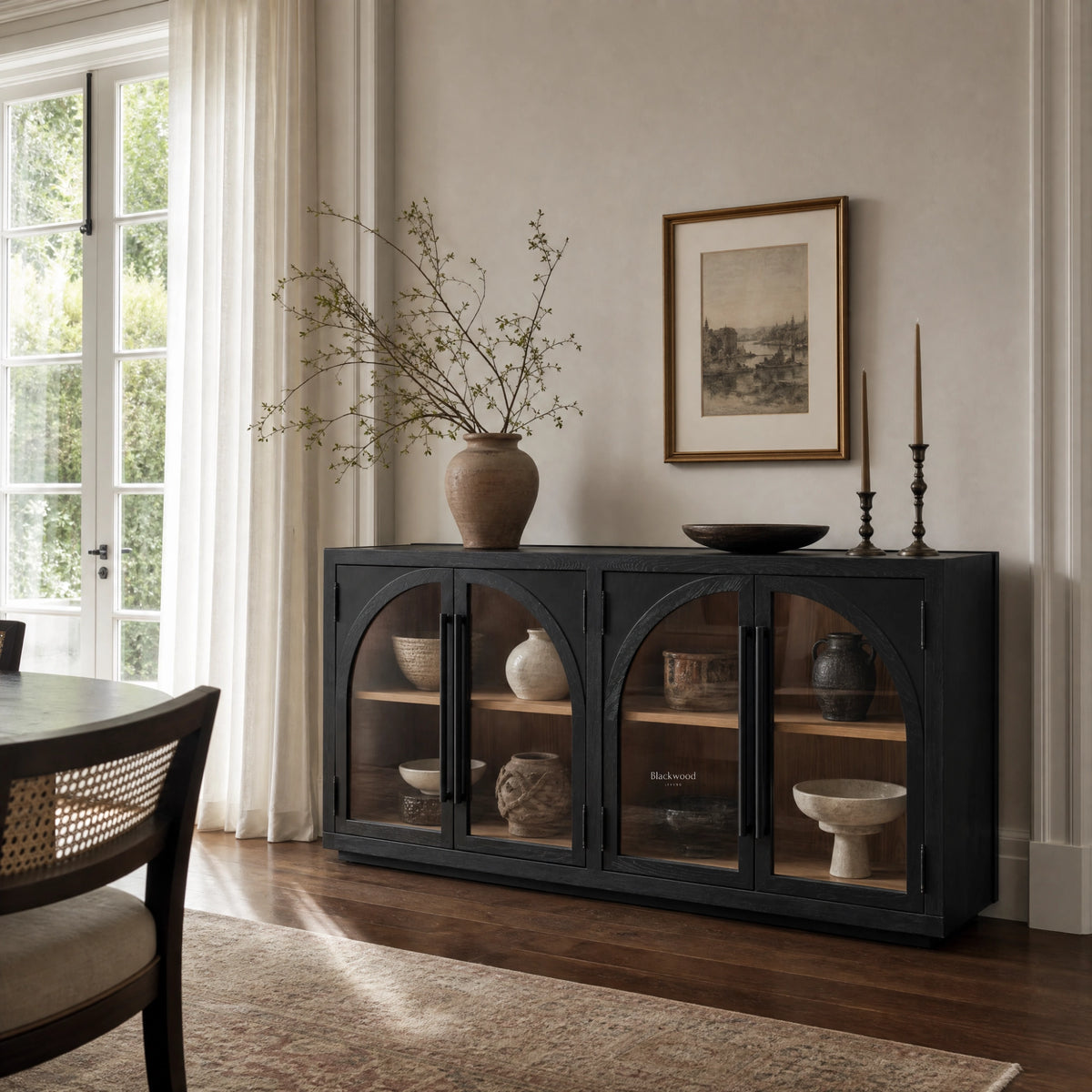 Dark elm sideboard with four arched glazed doors displaying ceramic vessels, styled with vase, bowl, and candles in a dining room.