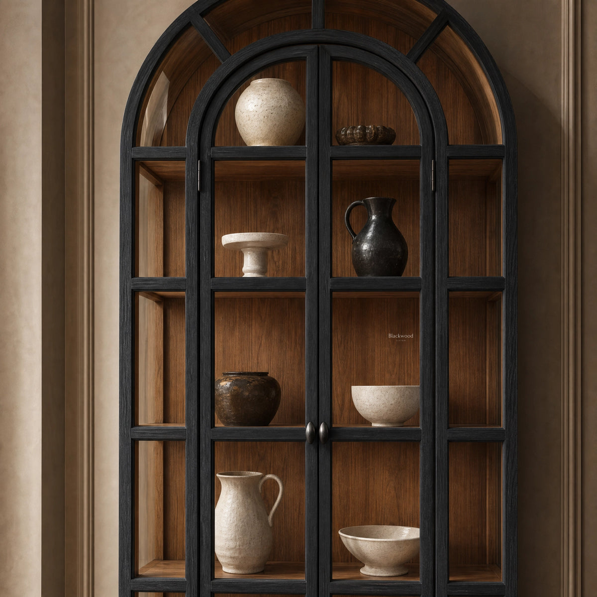 Arched glazed cabinet with dark frame and warm timber interior displaying ceramic vases and bowls. Heritage-style furniture.