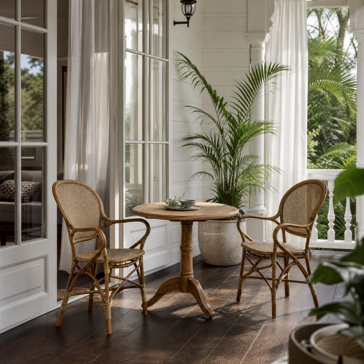 Sika Rossini Rattan Armchair - Antique on a covered porch with wicker chairs and a round table.