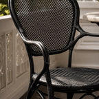 Black woven rattan armchair with a curved frame, detailed joints, and a diamond-pattern backrest.