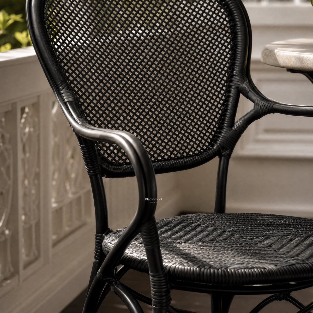 Black woven rattan armchair with a curved frame, detailed joints, and a diamond-pattern backrest.