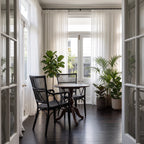 Black handmade rattan armchair with braided seat and vertical backrest beside a round table and potted plants in a sunlit room.