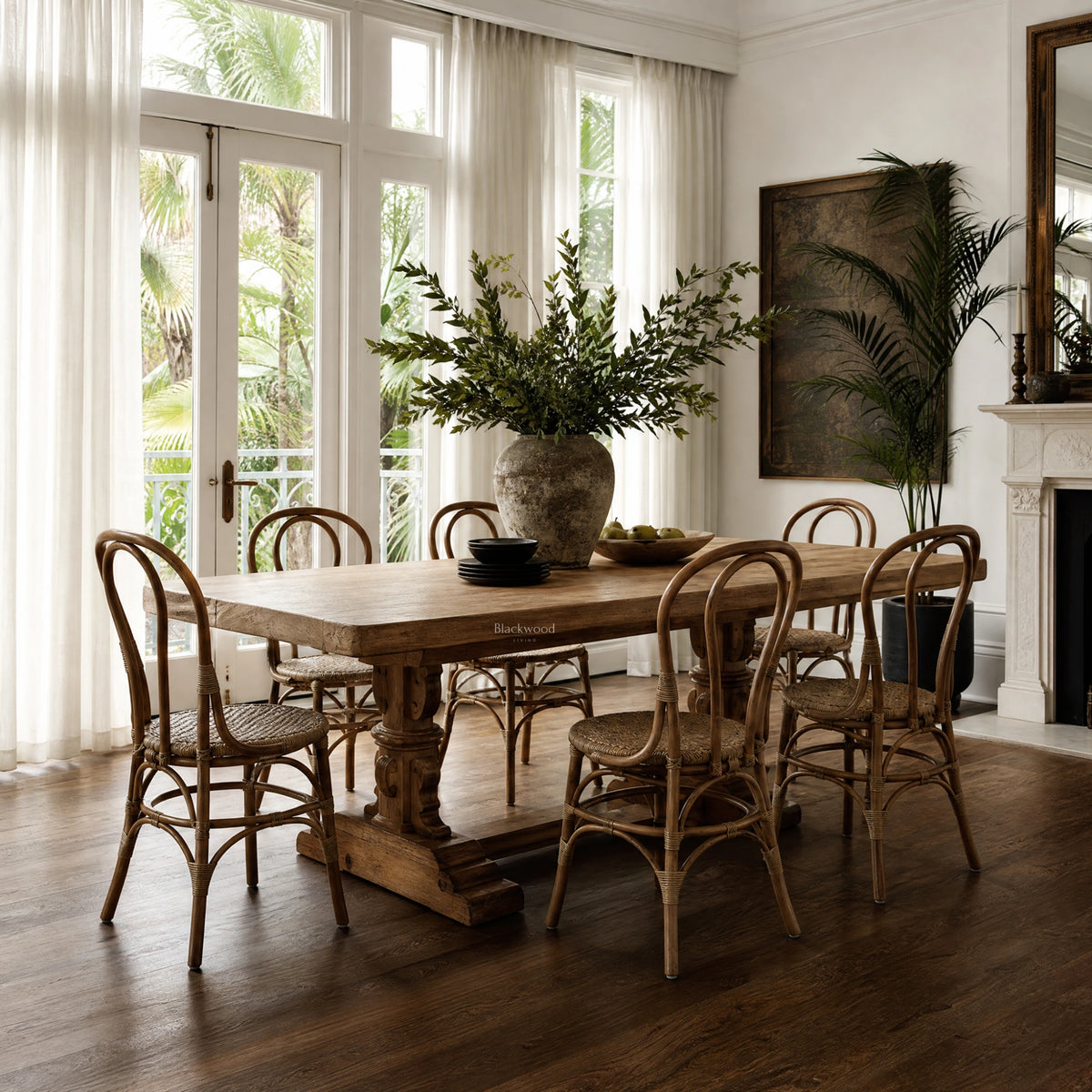 Sika Originals Lulu Rattan Side Chair arranged around a rustic wooden dining table in a sunlit room with French doors.
