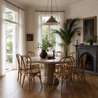 Sika Lulu rattan side chairs surround a stone dining table in a warm interior featuring a fireplace, large plants, and natural light.