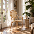 Rattan armchair with rounded back and woven panels placed on a wooden floor near sunlit curtains and a potted plant.