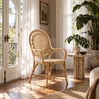 Rattan armchair with rounded back and woven panels placed on a wooden floor near sunlit curtains and a potted plant.