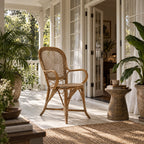 Sika Fleur rattan armchair with woven lattice back and curved arms on a bright porch lined with potted plants.