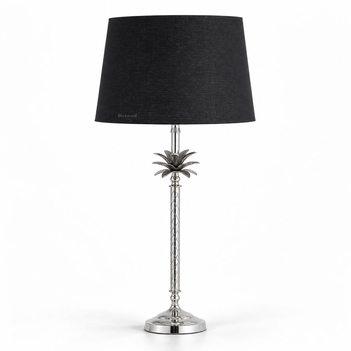 Tall polished metal table lamp with sculptural palm motif, diamond-patterned stem, and deep black linen shade.