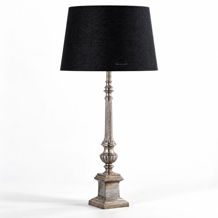 Tall table lamp with antique silver fluted stem, stepped pedestal base, and deep black cotton shade.