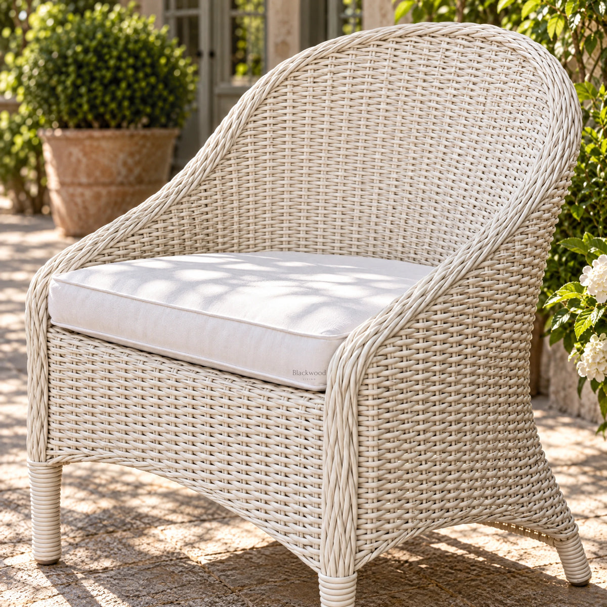 White outdoor rattan armchair with a sweeping woven profile and crisp white cushion, evoking a relaxed Mediterranean aesthetic on a sunny patio.