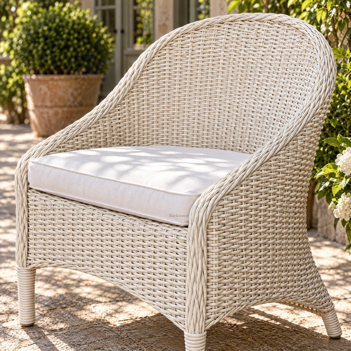 White outdoor rattan armchair with a sweeping woven profile and crisp white cushion, evoking a relaxed Mediterranean aesthetic on a sunny patio.