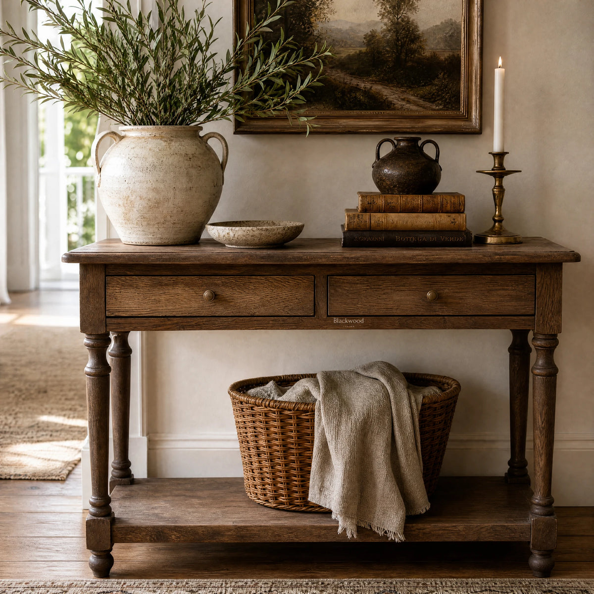 Bordeaux Hall Table in oak with natural grain, greenery vase, vintage pot, books, candle, landscape art, and basket.
