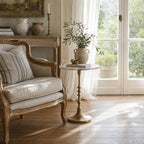 Round marble-top Marcel Side Table on an antique brass pedestal beside a striped sofa in a sunlit living room.
