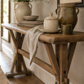 Bastille Console in reclaimed elm with a sturdy trestle base and rounded tabletop, paired with ceramic jars and books.
