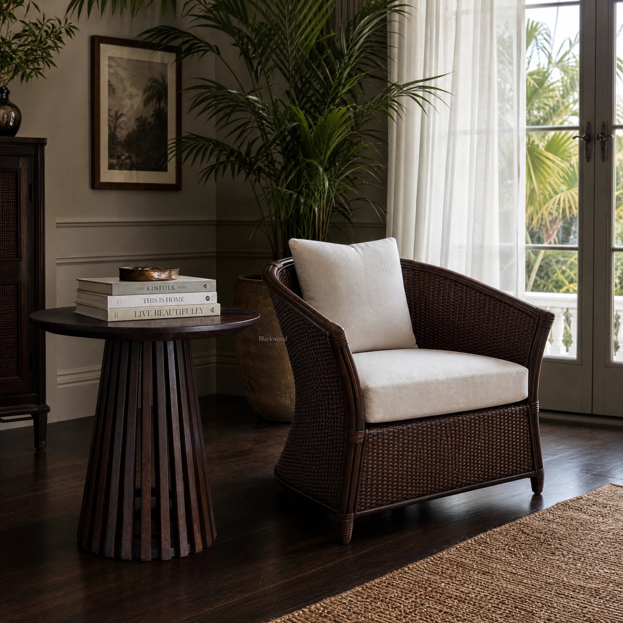 Banyan Side Table in cacao-stained solid oak with a slatted pedestal, set beside a wicker chair in a sunlit living room.
