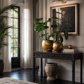 Taj Planters Set/2 in antiqued gold iron on a dark console with tropical plants.