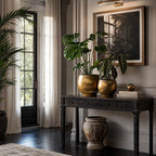 Taj Planters Set/2 in antiqued gold iron on a dark console with tropical plants.