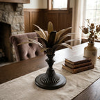Brass Palm Candle Holder with sculptural palm leaves on a dark pedestal, adding old-world warmth to a cozy living room.