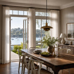 The Mercantile Brass Pendant in antique brass with aged finish hangs above a rustic dining table in a sunlit room.