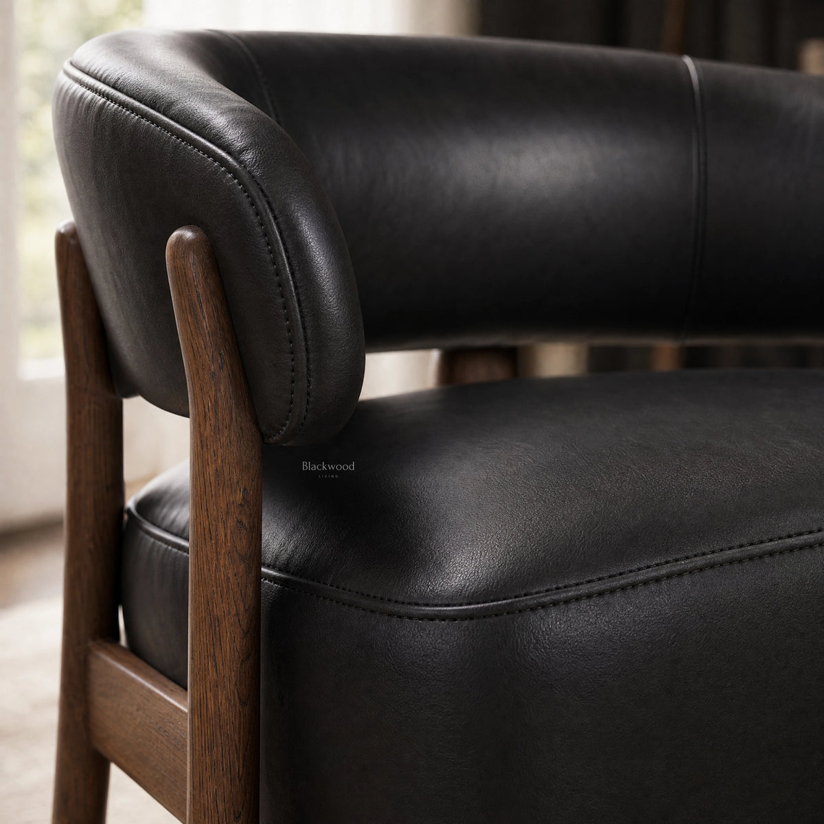 Black leather chair with curved back and solid ash timber frame, showcasing top grain texture and detailed stitching.