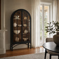 Tall black arched display cabinet with glazed doors and metal base holding neutral ceramic vessels.