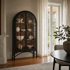 Tall black arched display cabinet with glazed doors and metal base holding neutral ceramic vessels.