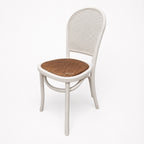 Whitehaven Dining Chair with white frame, caned back, and woven rattan seat.