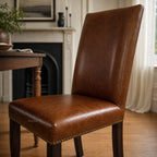 Manor Dining Chair in brown top-grain cowhide leather with brass nailhead trim and dark wood legs.