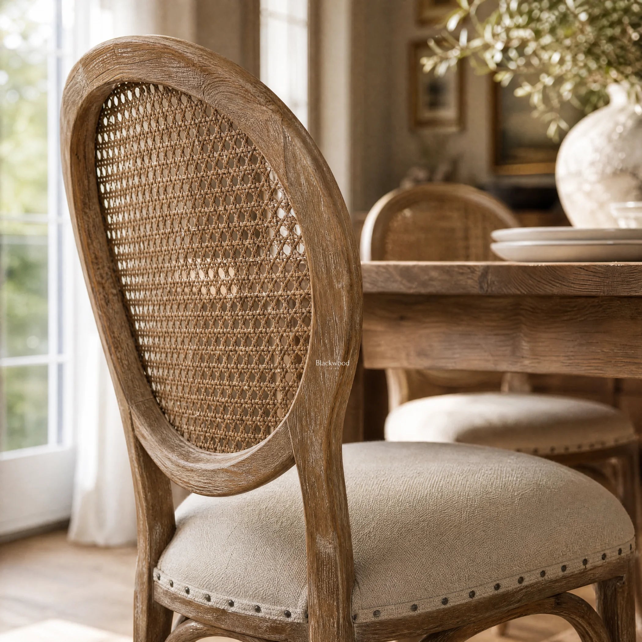 Camille Dining Chair with burnt oak, handwoven rattan back, and linen upholstered seat in French Provincial style.
