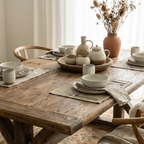 Foundry Dining Table, recycled elm, in a sunlit dining room with ceramic dinnerware and a vase of dried stems.
