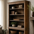 Wycliffe Bookcase in warm recycled-pine finish with books, ceramic pots, framed art, and nearby greenery.