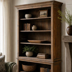 Wycliffe Bookcase in warm recycled-pine finish with books, ceramic pots, framed art, and nearby greenery.