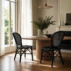 Sika® Rossini Rattan Side Chair - Black around a round grooved-wood table in a bright dining room.