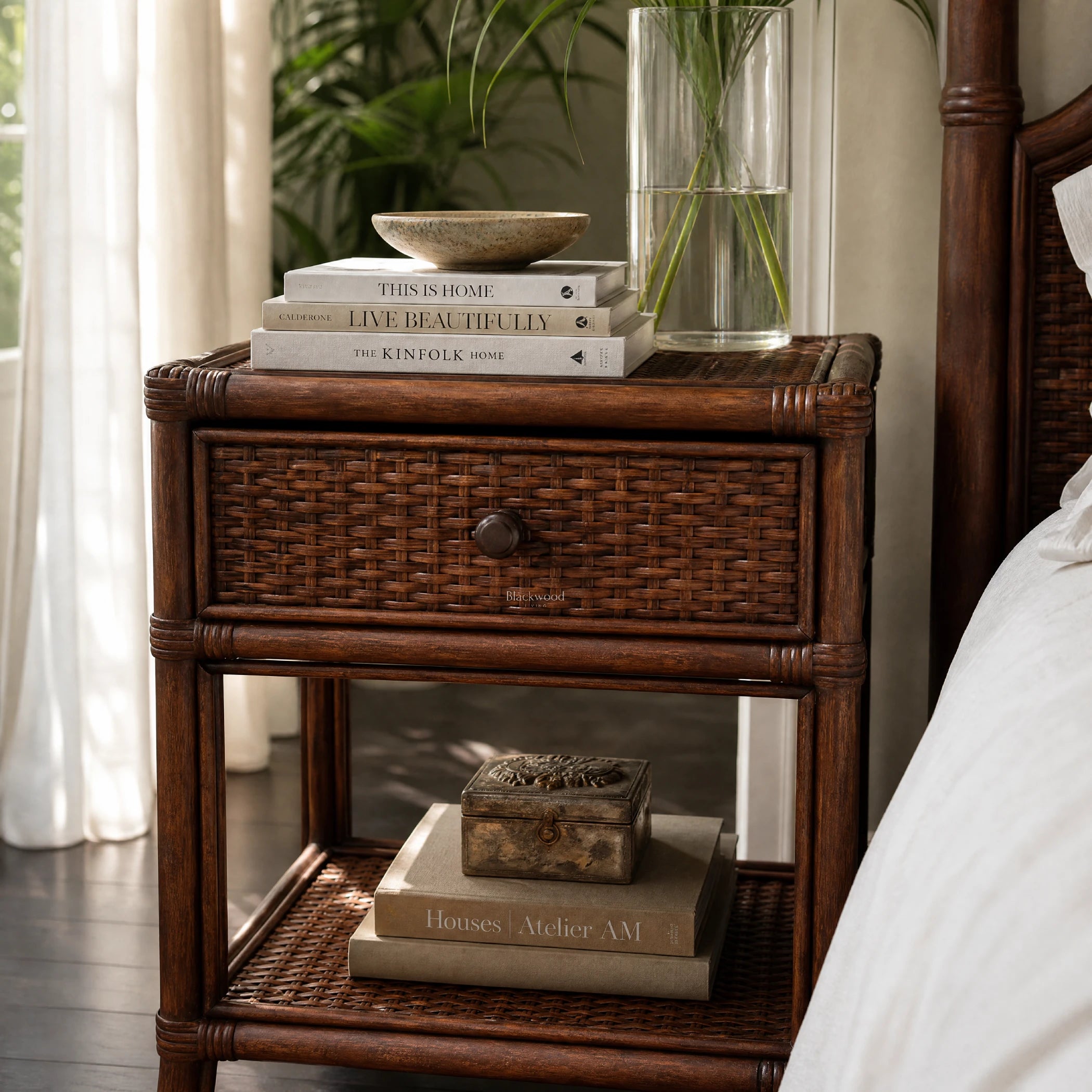 Plantation 1 Drawer Bedside with woven rattan, featuring a ceramic bowl atop stacked books and a glass vase of greenery.