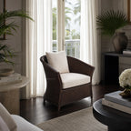 Havana Lounge Chair in cacao wicker with a cream cushion by a window, surrounded by tropical plants.