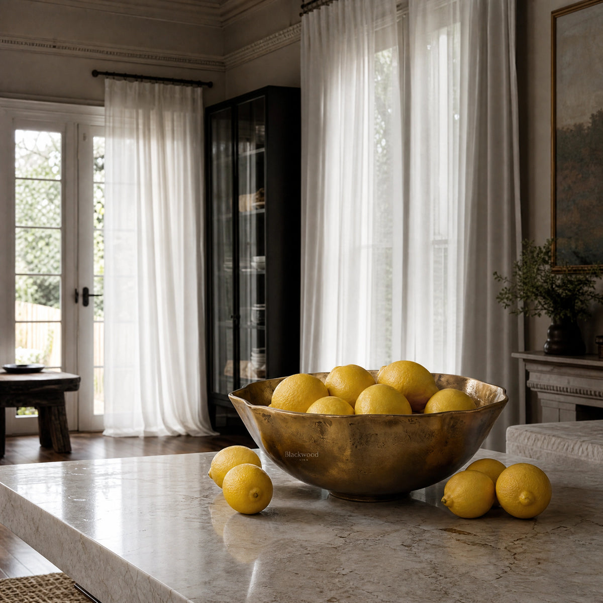 Ankara Gilded Poppy Bowl, undulating aluminium with brass finish and aged patina, holding lemons on a marble island.