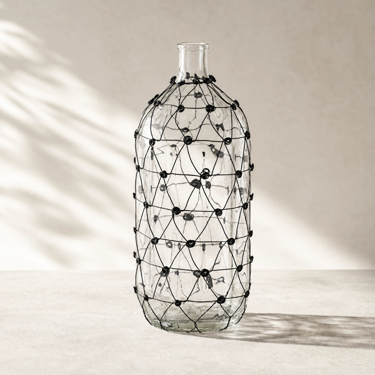Salvage wired glass vase with wrapped black wire lattice on clear glass.