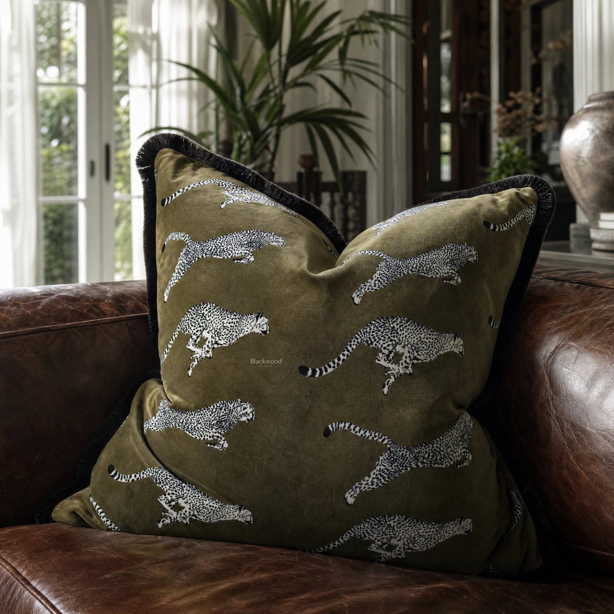 Leopard Velvet Cushion Cover 55cm with leopard silhouettes on olive-green velvet, placed on a brown leather sofa.