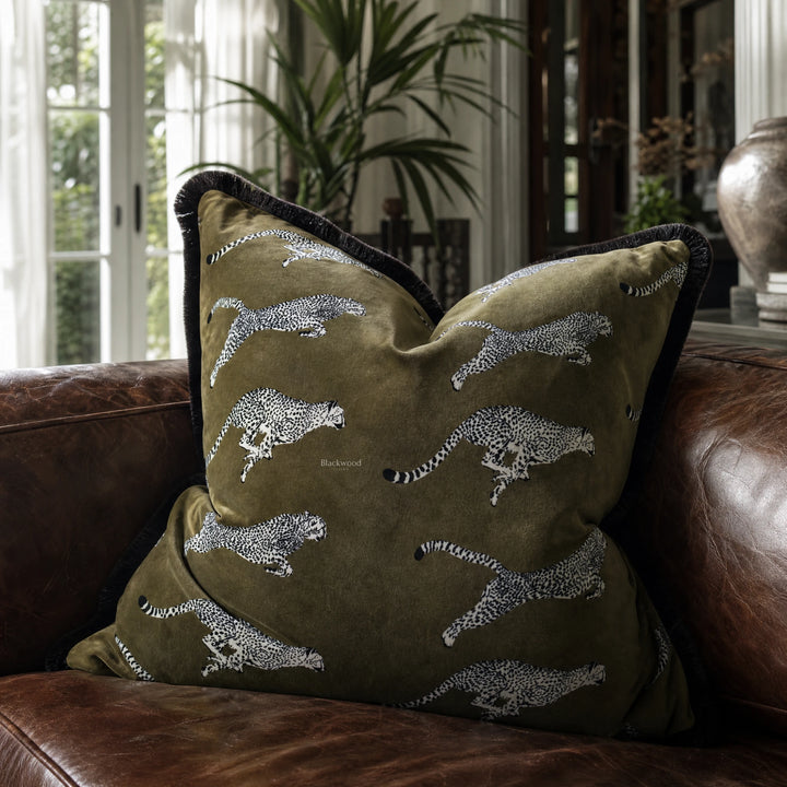 Leopard Velvet Cushion Cover 55cm with leopard silhouettes on olive-green velvet, placed on a brown leather sofa.