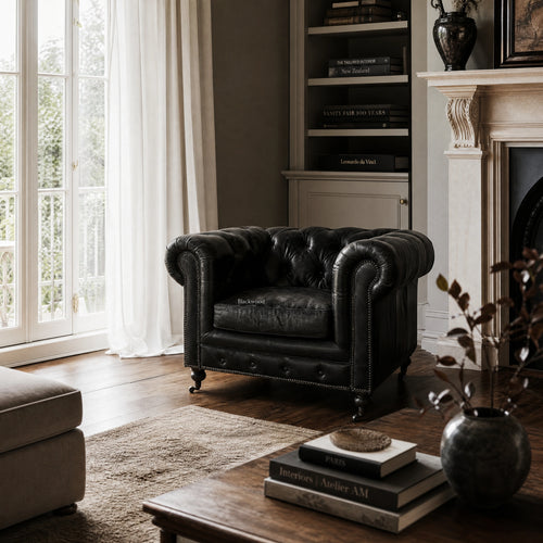 Ashcroft Armchair in estate black leather with Chesterfield tufting in a living room by bookshelf and fireplace.
