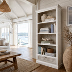 Whitehaven Bookcase in antique white mango wood with layered texture, filled with books in a coastal living room.