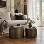 Foundry Table Duo coffee tables in antique gold iron with hammered finish sit beside a beige sofa.
