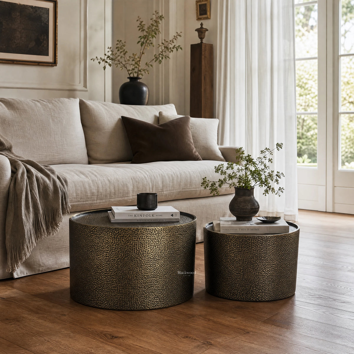 Foundry Table Duo coffee tables in antique gold iron with hammered finish sit beside a beige sofa.