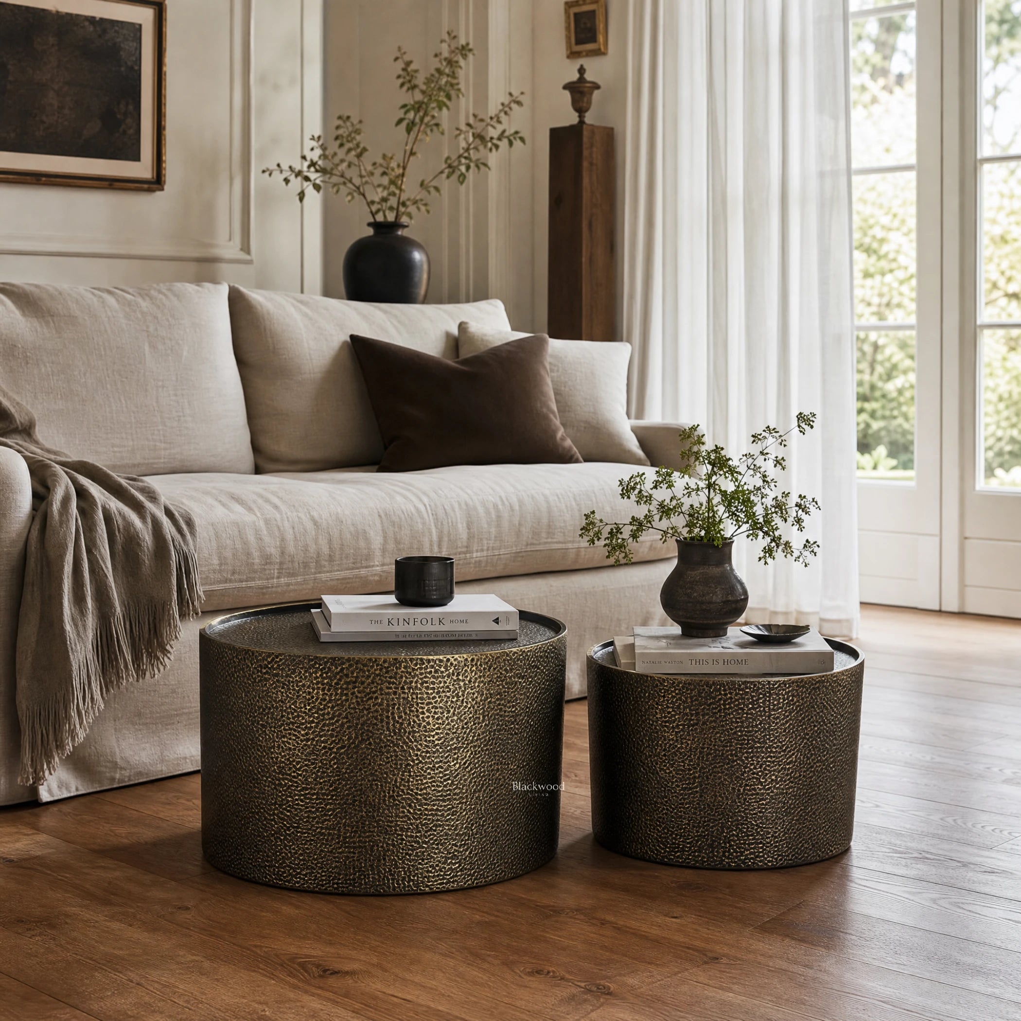 Foundry Table Duo coffee tables in antique gold iron with hammered finish sit beside a beige sofa.