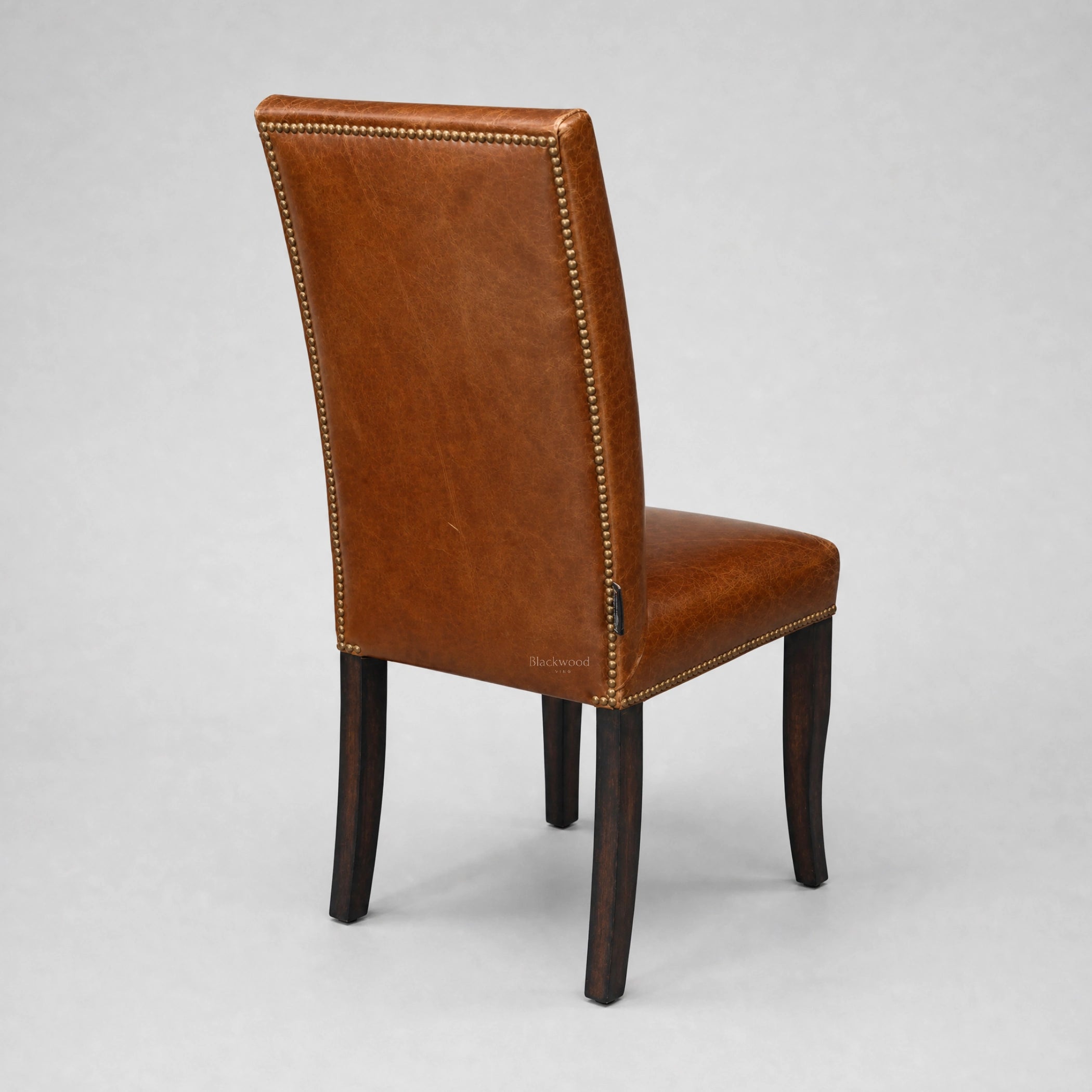 Manor Dining Chair in brown top-grain cow leather with brass stud trim and dark wood legs.