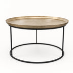 Round antique brass coffee table with raised tray edge and slender black iron frame for plantation-inspired interiors.