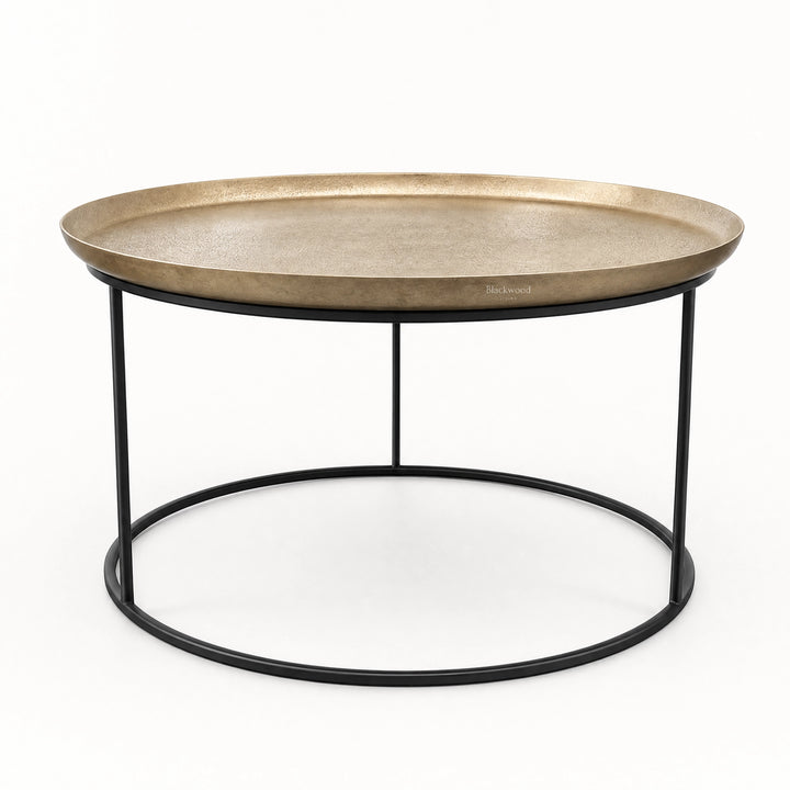 Round antique brass coffee table with raised tray edge and slender black iron frame for plantation-inspired interiors.