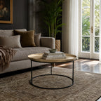Round antique brass coffee table with slender black iron frame. Plantation-inspired design with raised tray top and stack of books.