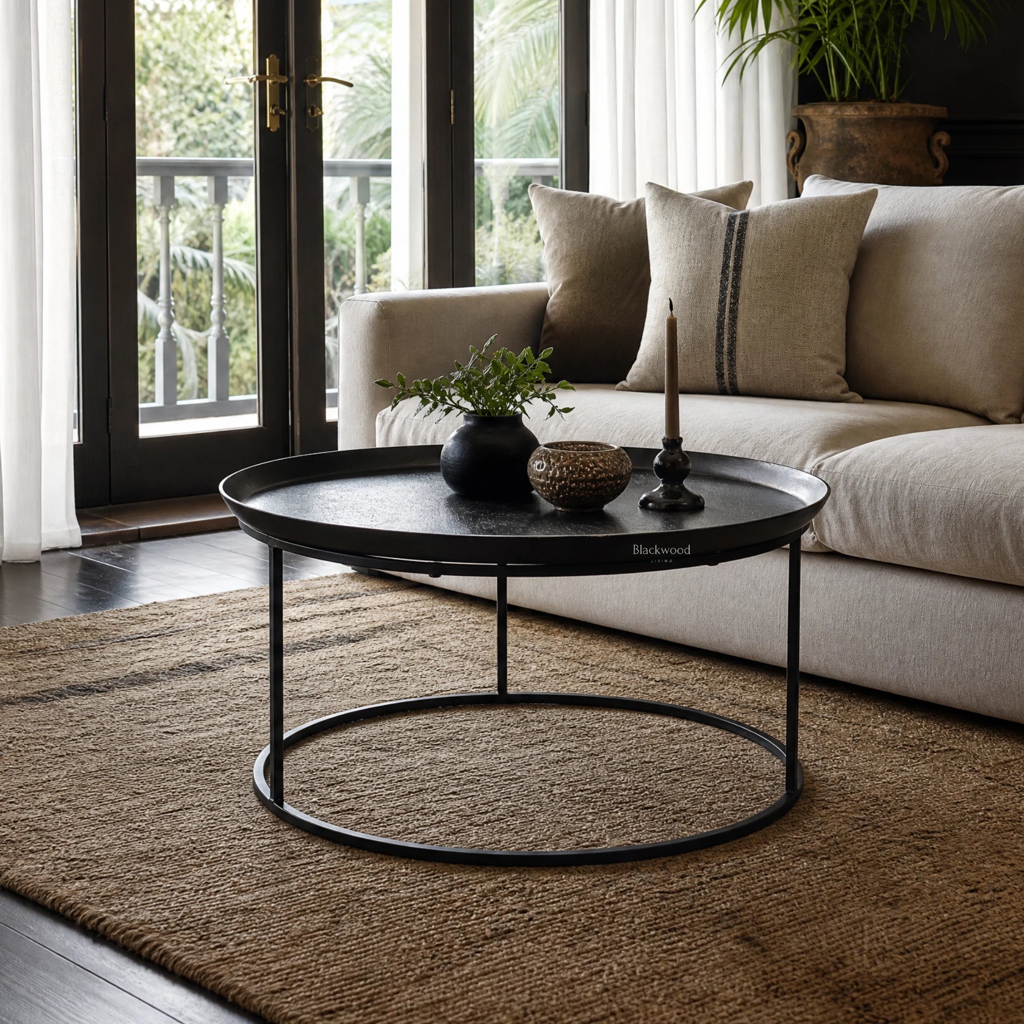 Round antique black coffee table with raised metal tray top and slender iron frame in a living room setting.