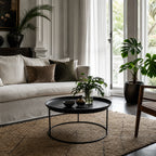 Round antique black coffee table with raised tray edge and slender iron frame in a plantation-style living room.